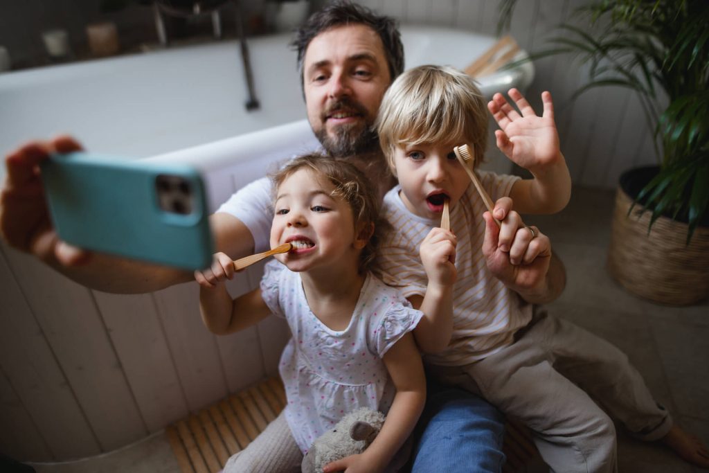 A man and two children brushing their teeth.
