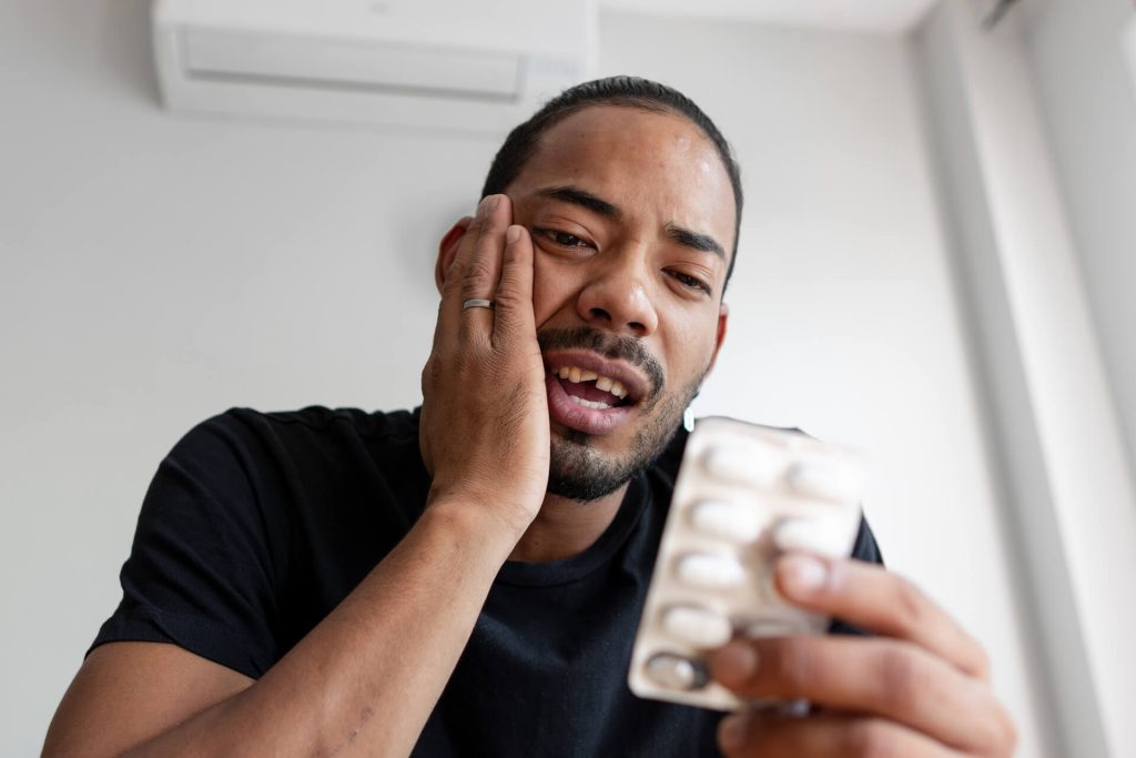 A man with a broken tooth is getting ready to take a pain reliever.